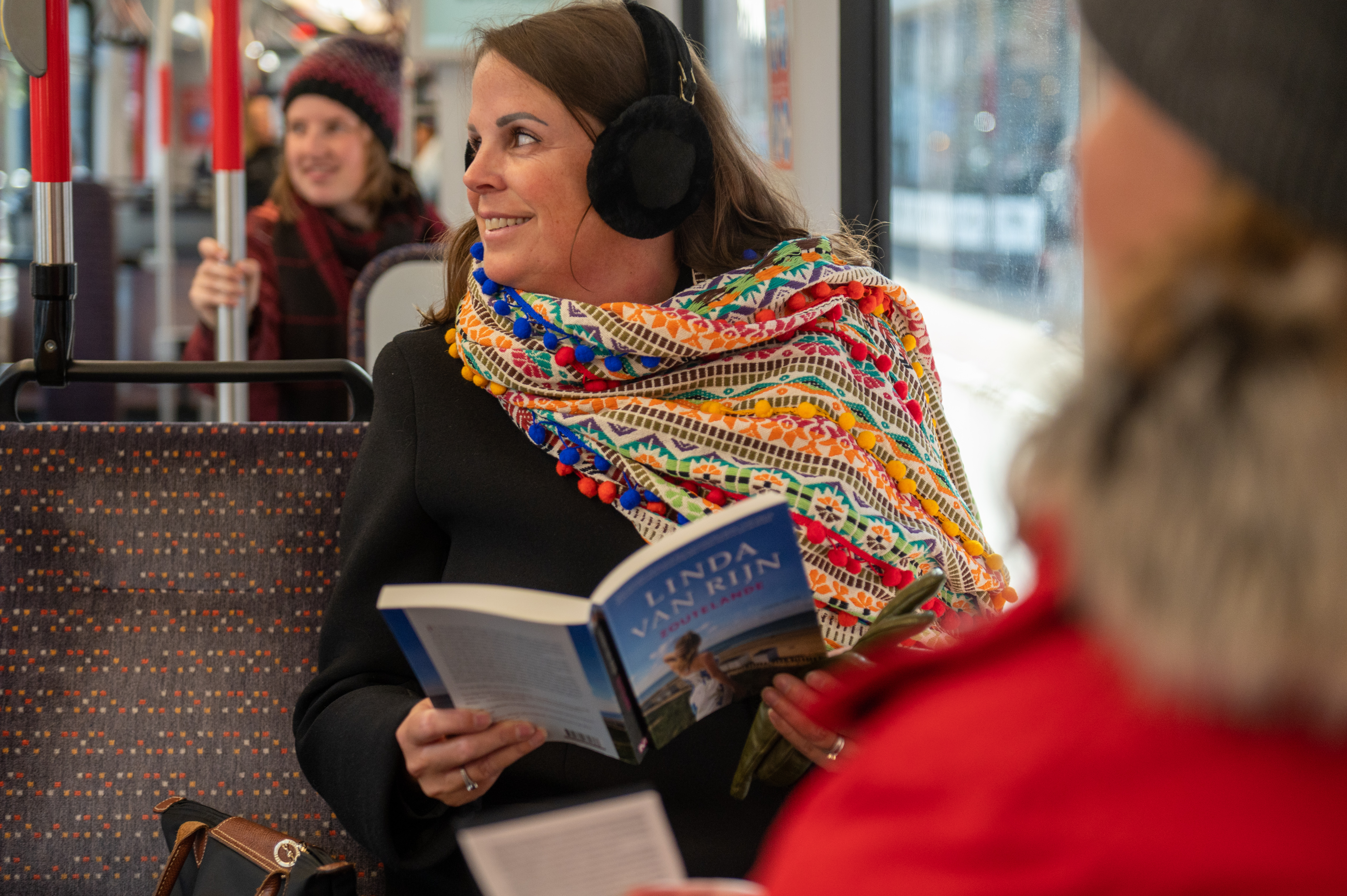 Vrouw leest boek in HTM tram en heeft oorwarmers op
