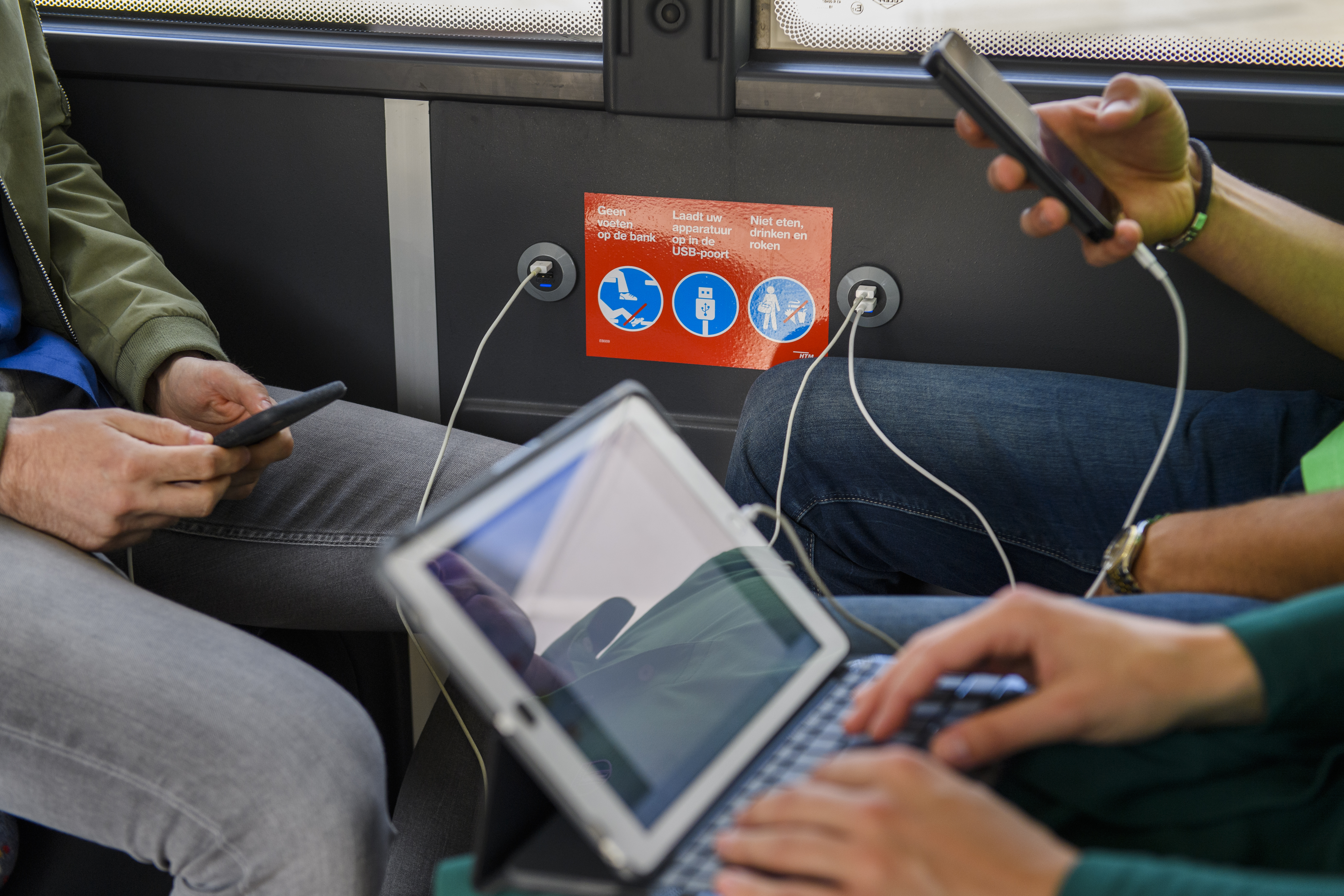 Reizigers laden telefoons en tablet op in HTM bus