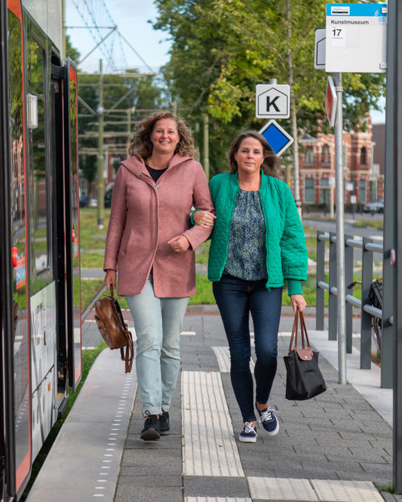 Reizigers lopen op tramhalte Reizigers lopen op halte naast HTM tram en kijken naar de camera