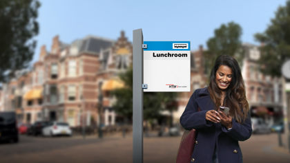 HTM | Zakelijk geklede vrouw staat op een HTM halte en kijkt naar haar telefoon HTM | Zakelijk geklede vrouw staat op een HTM halte en kijkt naar haar telefoon