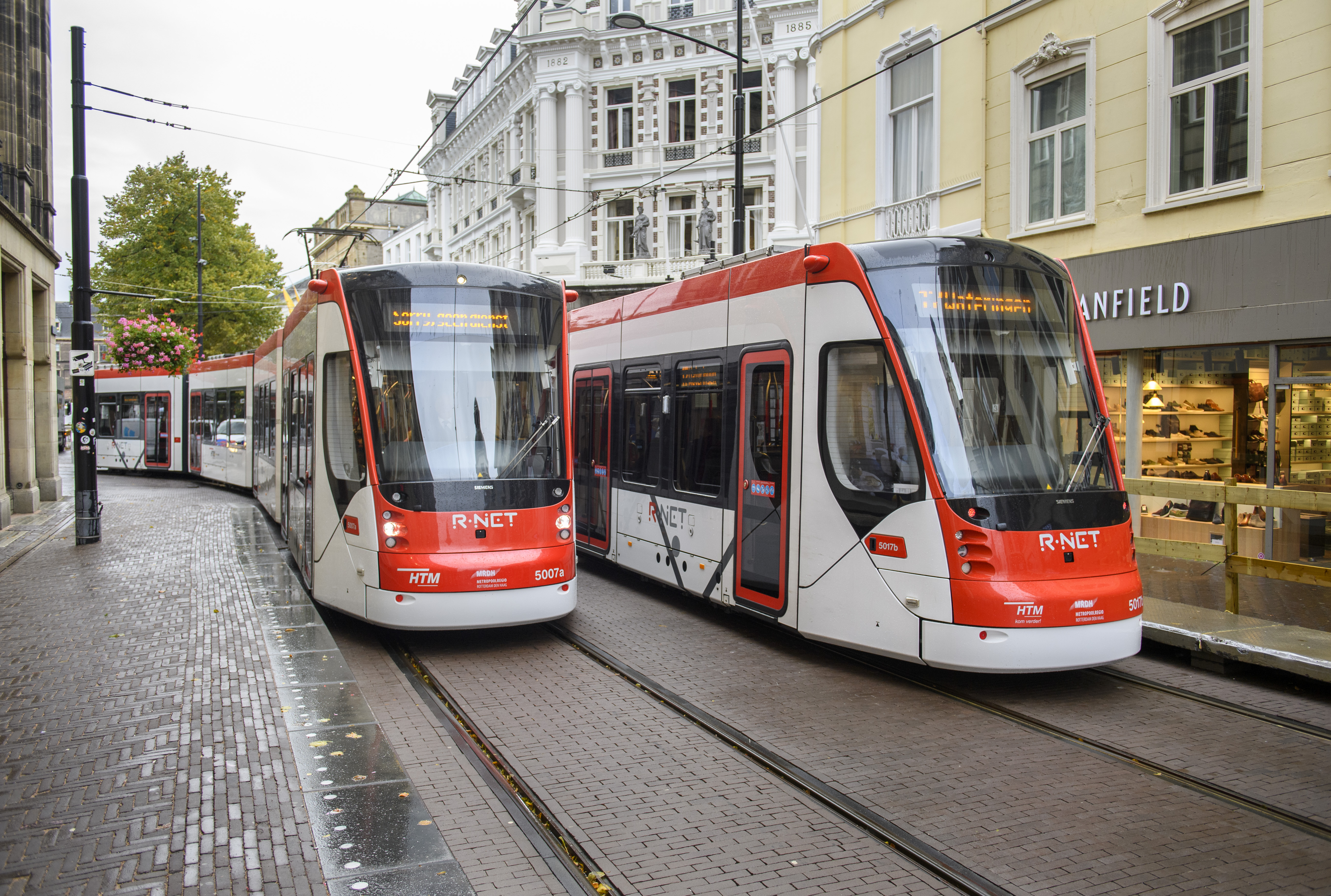 Twee HTM trams langs naast elkaar langs winkels in Den Haag