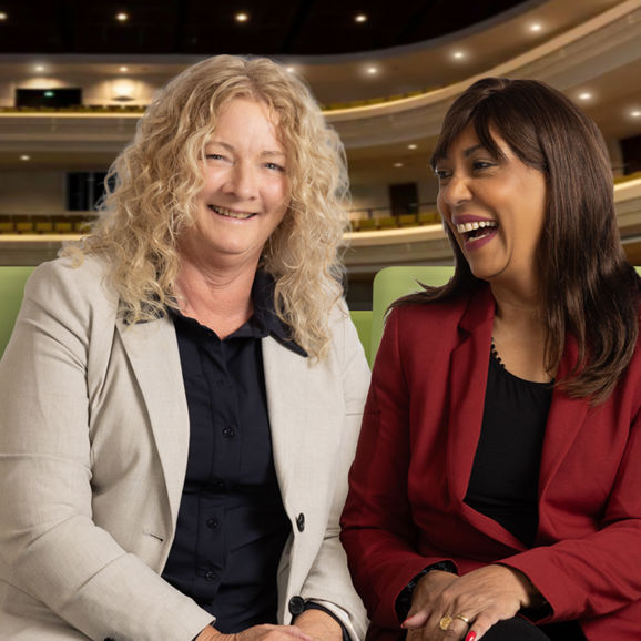 Twee vrouwen zitten gezellig in het theater lachend naar elkaar Twee vrouwen zitten gezellig in het theater lachend naar elkaar